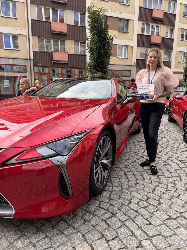 Kobieta trzyma ulotkę LSSE, stoi przy czerwonym aucie